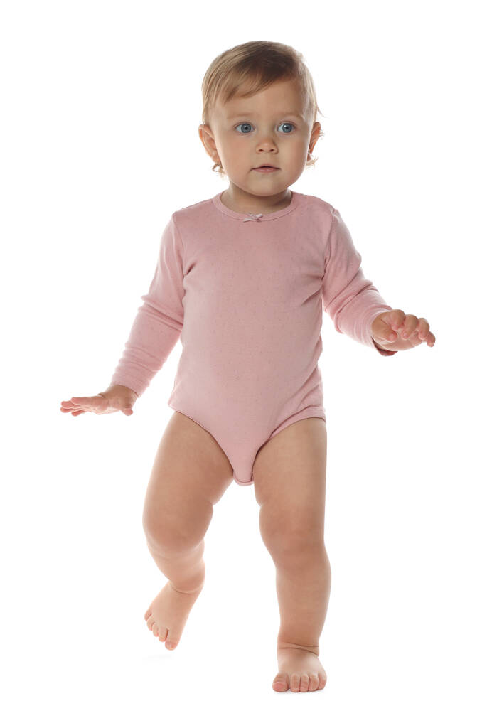 Cute baby girl in pink bodysuit learning to walk on white background - Zdjęcie, obraz