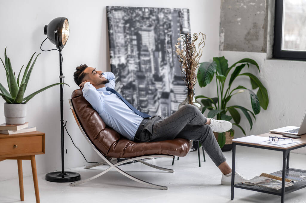 Time for yourself. Business young bearded man with closed eyes smiling vacationer sitting in leather chair sideways to camera - Fotoğraf, Görsel
