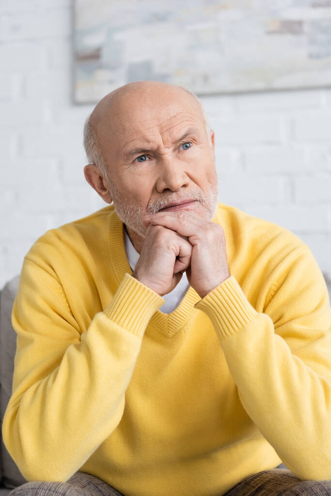 Displeased senior man looking away in living room  - Fotó, kép