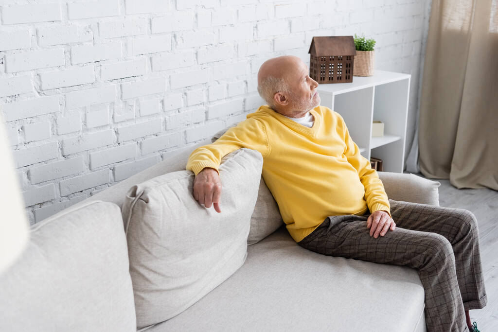 Πλευρική άποψη του ηλικιωμένου άνδρα που κάθεται στον καναπέ στο σπίτι  - Φωτογραφία, εικόνα