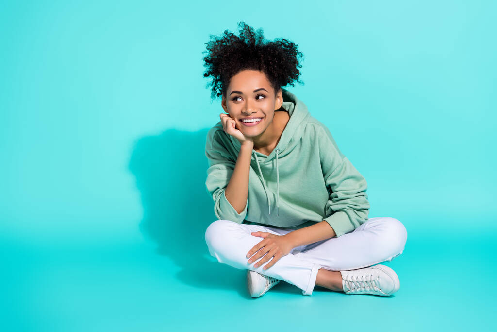 Full length photo of excited sweet lady wear sweatshirt looking empty space arm chin isolated turquoise color background. - 写真・画像