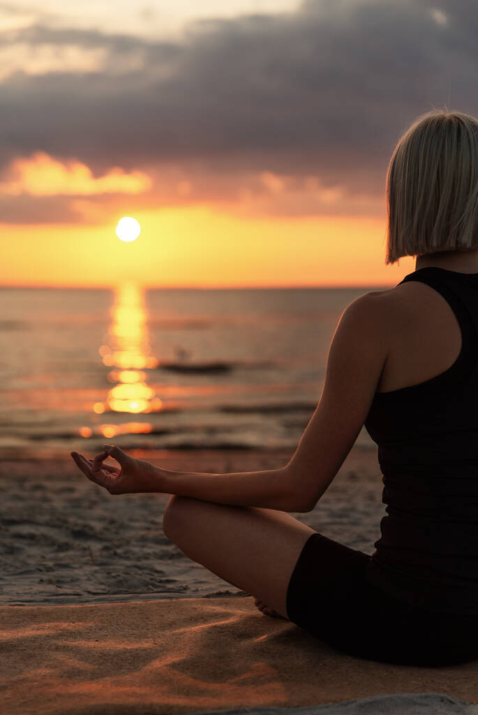 yoga, mindfulness and meditation concept - woman meditating in lotus pose on beach over sunset - Fotografie, Obrázek