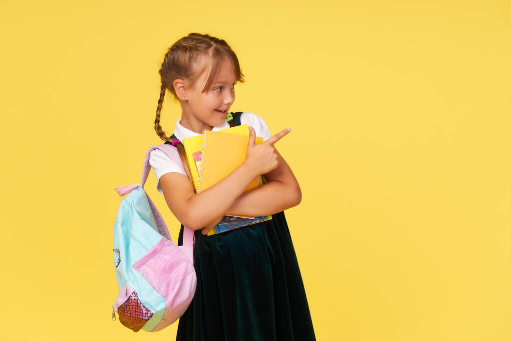 Portret van een schoolmeisje met lesboeken en een rugzak op een gele achtergrond. Terug naar school - Foto, afbeelding