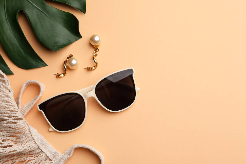 Νέα κομψά γυαλιά ηλίου, όμορφα σκουλαρίκια και τσάντα σε μπεζ φόντο, επίπεδη lay. Χώρος για κείμενο - Φωτογραφία, εικόνα