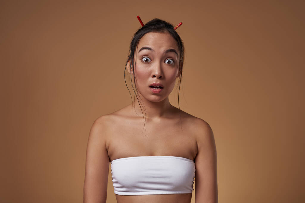 Scared or surprised stylish asian girl looking at camera. Attractive young brunette woman wearing tank top. Female beauty. Isolated on orange background. Studio shoot. Copy space - Photo, Image