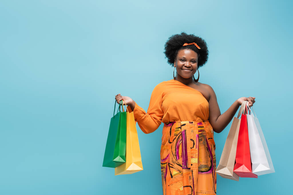 happy african american body positive woman holding shopping bags isolated on blue - Fotoğraf, Görsel