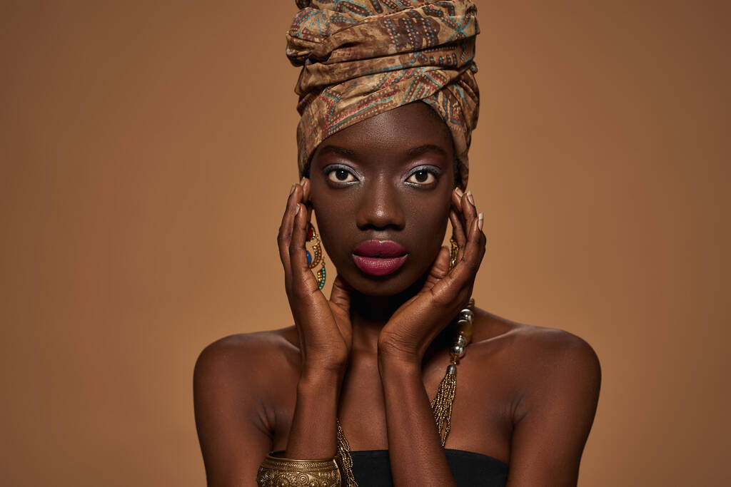 Περικονιασμένο από αυτοπεποίθηση κομψό μαύρο κορίτσι φορώντας παραδοσιακή αφρικανική στολή και αξεσουάρ κοιτάζοντας κάμερα. Ελκυστική νεαρή λεπτή γυναίκα. Απομονωμένο σε πορτοκαλί φόντο. Γυρίζουμε στούντιο. Αντιγραφή χώρου - Φωτογραφία, εικόνα