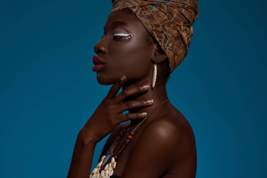 Cropped side view of elegant black girl wearing traditional national african outfit and accessories. Beautiful young slim woman. Female beauty. Isolated on blue background. Studio shoot. Copy space - Fotografie, Obrázek