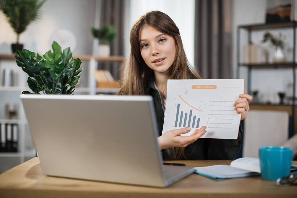Smiling female manager leading working meeting through video call on laptop. Young woman freelance showing graphs and chart while sitting at table. - Foto, Imagem