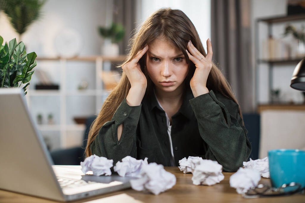 Кавказская молодая женщина подчеркнул о работе в домашнем офисе и посмотреть на что-то на экране ноутбука, стресс дал ей огромную головную боль. - Фото, изображение