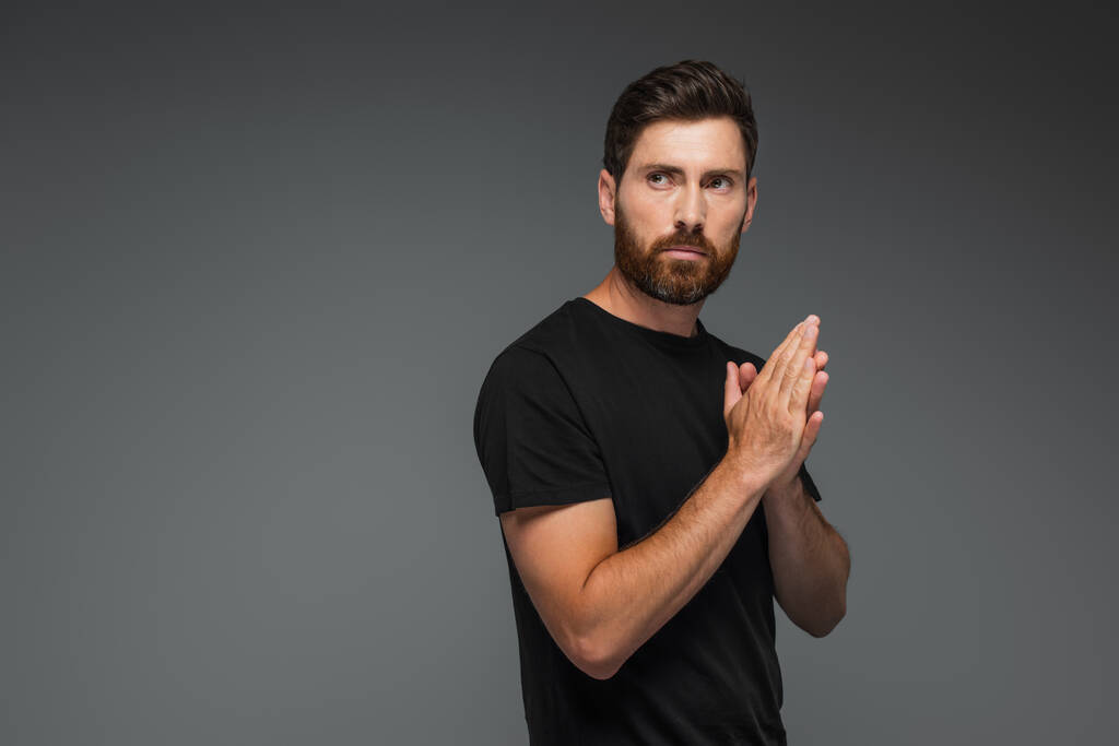 portrait of confident and bearded man in black t-shirt looking away isolated on grey - Foto, Imagem
