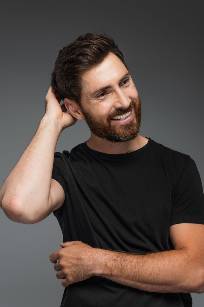 portrait of pleased man in black t-shirt looking at camera isolated on grey - Fotografie, Obrázek
