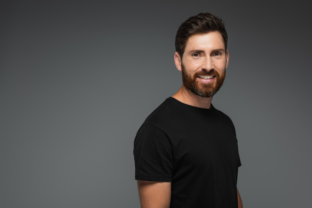 portrait of smiling bearded man in black t-shirt looking at camera isolated on grey - Fotografie, Obrázek