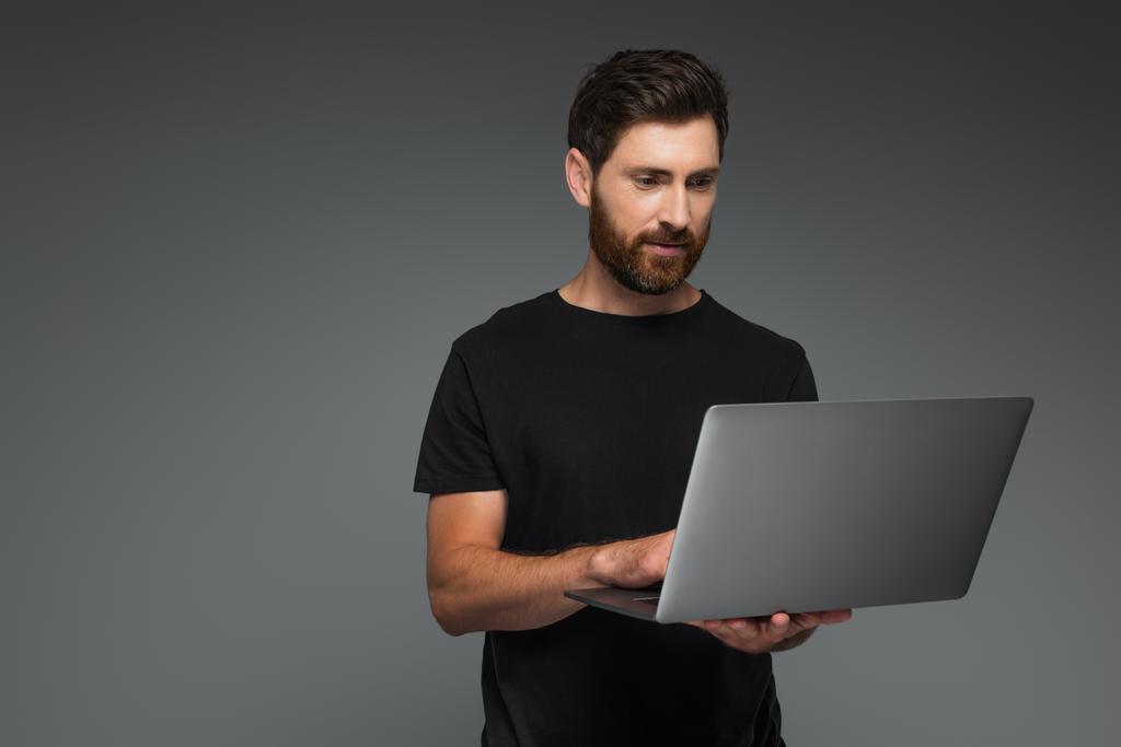 bearded man in black t-shirt using laptop isolated on grey - 写真・画像