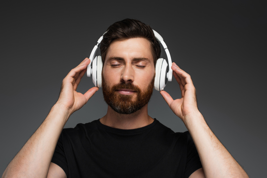bearded man in wireless headphones listening music isolated on grey - Fotó, kép
