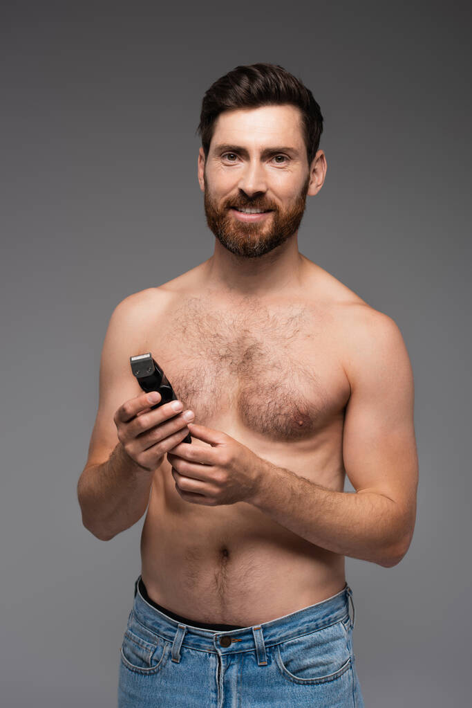 happy and shirtless man with hair on chest holding electric razor isolated on grey - Photo, Image