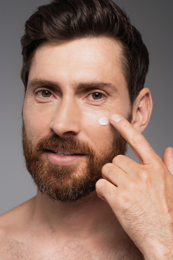 close up of man with beard applying cream on face isolated on grey - Fotografie, Obrázek