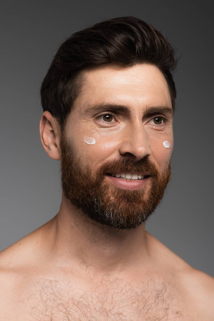 portrait of bearded man with cream on face smiling isolated on grey - Foto, afbeelding