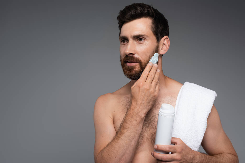 bearded man with towel applying shaving foam isolated on grey - Zdjęcie, obraz