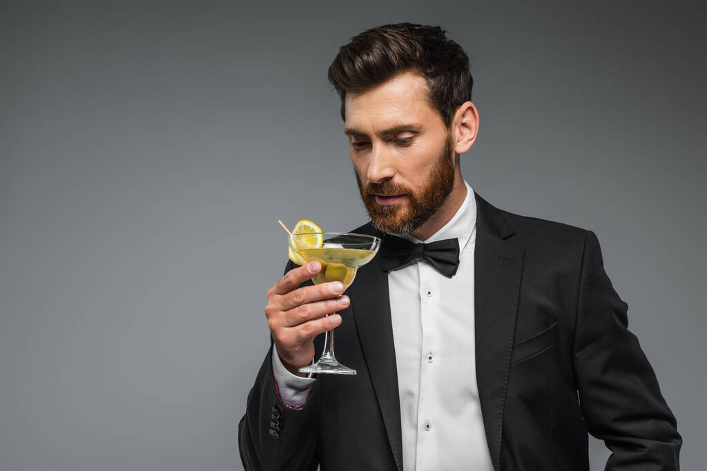 bearded man in suit looking at glass with cocktail isolated on grey - Fotoğraf, Görsel