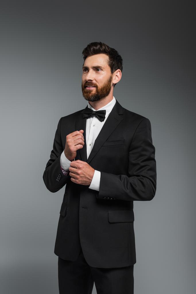 smiling man with beard standing in elegant suit with bow tie isolated on grey  - Foto, Imagem