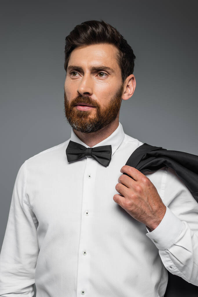 portrait of bearded man in suit with bow tie holding blazer isolated on grey  - Photo, image