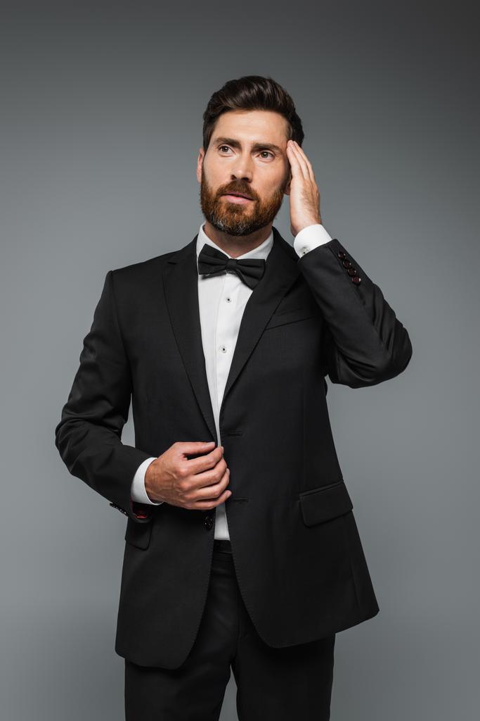 elegant man in suit with bow tie adjusting hair isolated on grey - Photo, Image