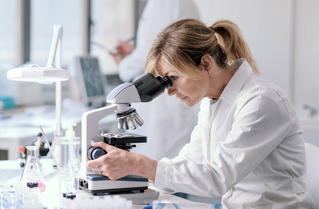 Woman working in a medical laboratory, she is using a microscope - Valokuva, kuva
