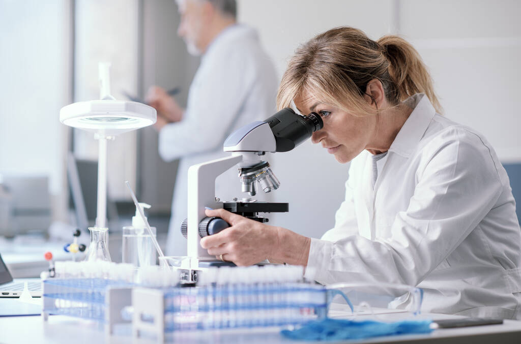 Женщина, работающая в медицинской лаборатории, использует микроскоп - Фото, изображение