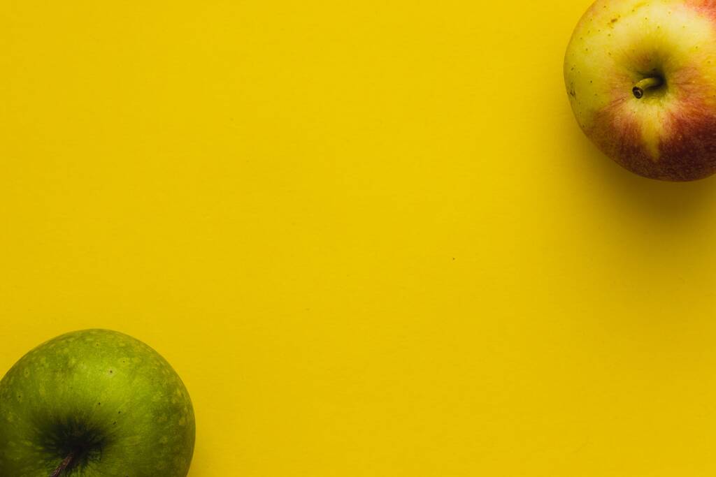Een bovenaanzicht van groene en geel-rode appels in de tegenoverliggende hoeken op een gele achtergrond - Foto, afbeelding