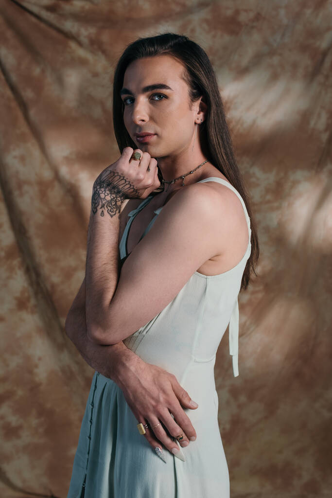 Young queer person in sundress looking at camera on abstract background  - Photo, Image