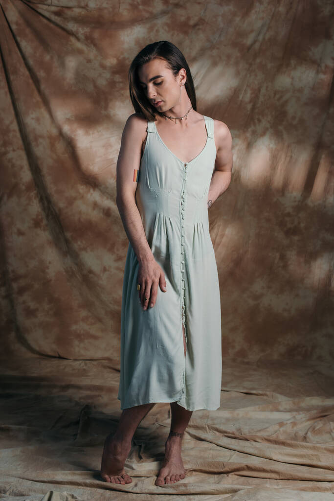 Barefoot queer person in sundress standing on abstract brown background  - Zdjęcie, obraz