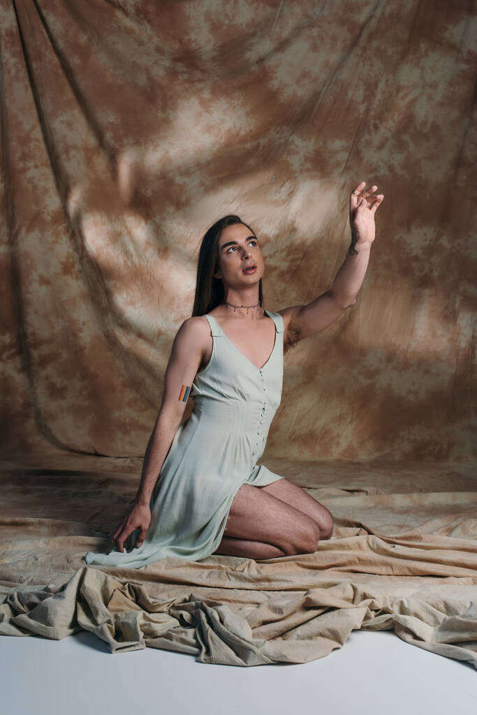 Nonbinary person in sundress sitting and gesturing on abstract brown background  - Foto, immagini