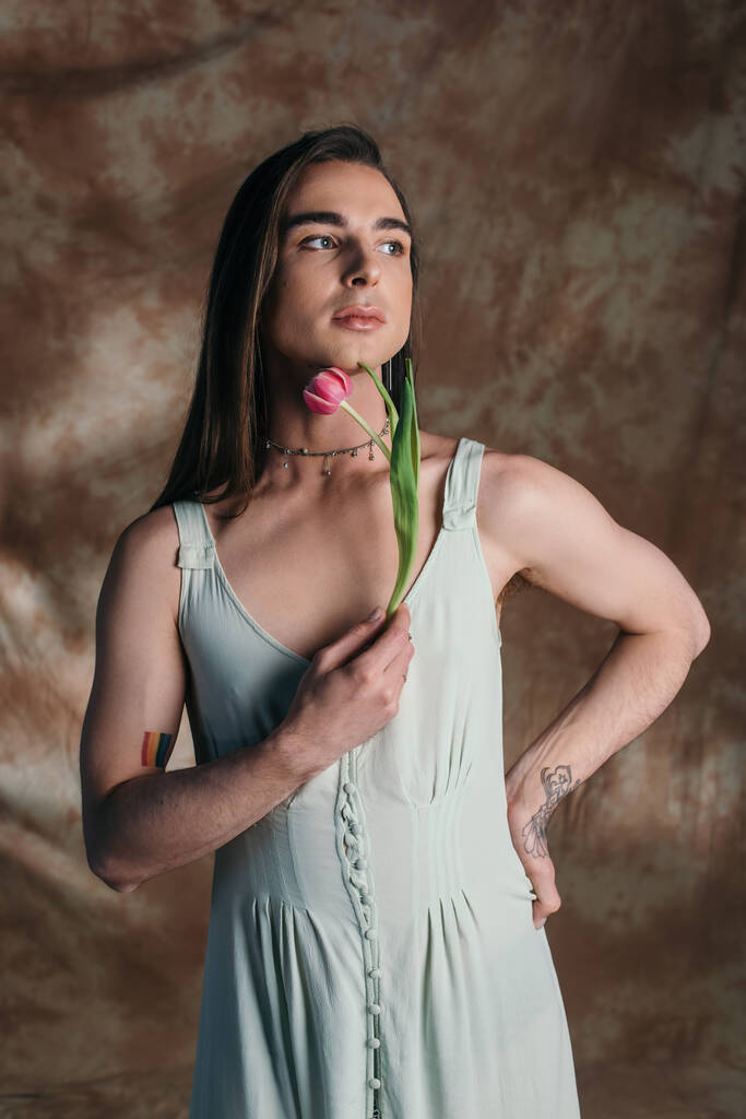 Brunette nonbinary person in sundress holding tulip on abstract brown background  - Fotó, kép