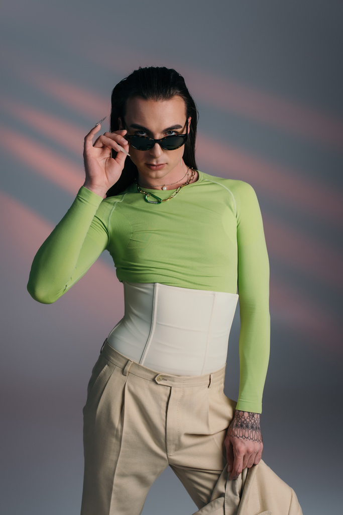 Young queer model holding sunglasses and jacket on abstract background  - Fotoğraf, Görsel