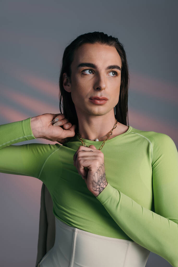 Trendy nonbinary model touching necklace and looking away on abstract background  - Foto, imagen
