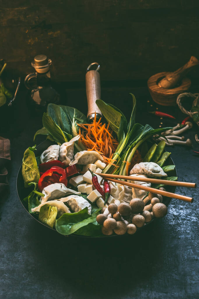 Tasty vegetarian Asian dumpling hot pot. Fresh colorful Asian food ingredients in wok pan with chopsticks on dark rustic kitchen table background. - Foto, Bild