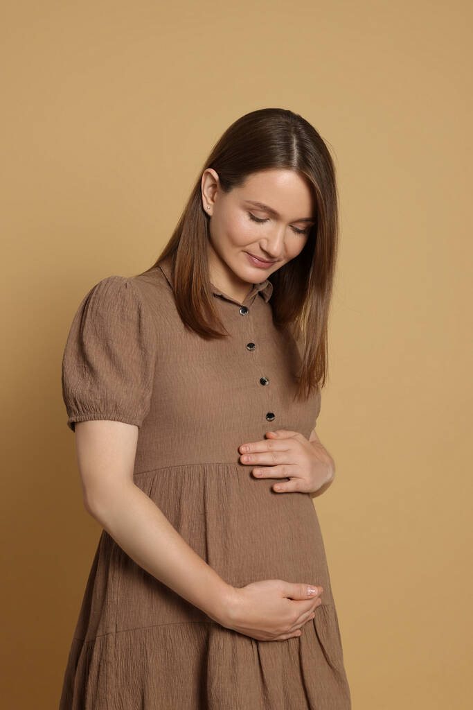 Happy young pregnant woman on light brown background - Fotografie, Obrázek