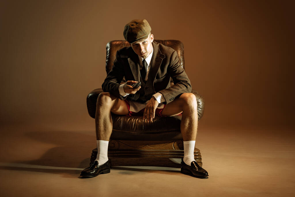 Challenge. Cinematic portrait of young man, retro 1920s style english gangster wearing suit and cap isolated on dark brown background. Concept of business, personality, emotions, family, art, fashion - Fotó, kép