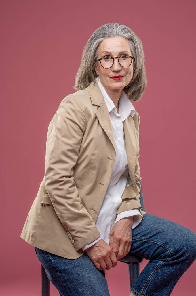 Elegant woman. Elegant mature woman in beige jacket sitting on a chair - Fotó, kép