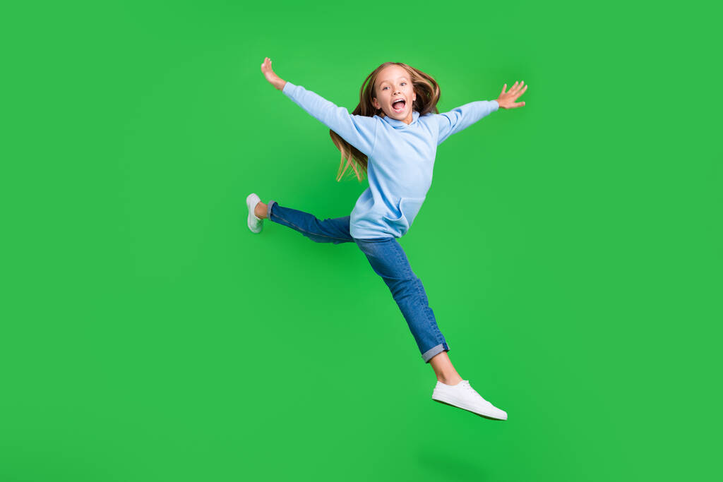 Full length φωτογραφία του σπορ αξιολάτρευτο μικρό κορίτσι άλμα χέρια εξάπλωση έχουν τη διασκέδαση φορούν κομψό μπλε αθλητικά ρούχα που απομονώνονται σε πράσινο χρώμα φόντο. - Φωτογραφία, εικόνα