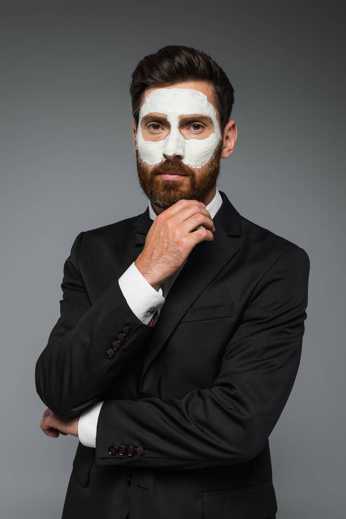 portrait of bearded man in suit with clay mask on face isolated on grey  - Foto, imagen