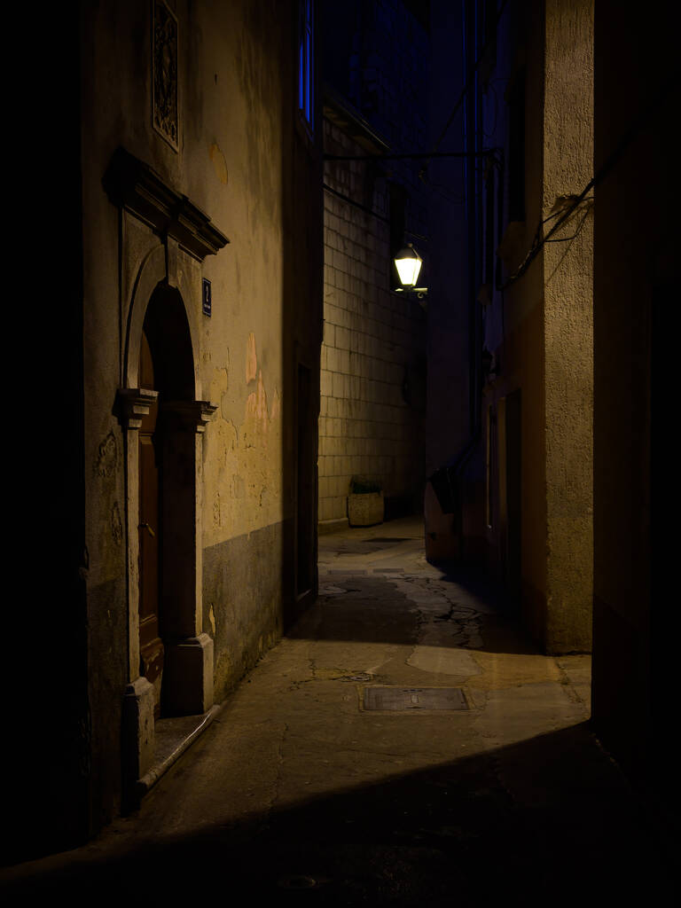 Cres, Croatia - April 11, 2022: Narrow street in Cres with old streetlamps during night - 写真・画像