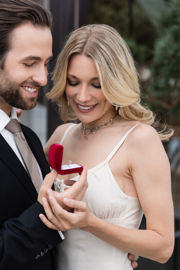 Smiling man in suit holding box with engagement ring near girlfriend outdoors  - Photo, image