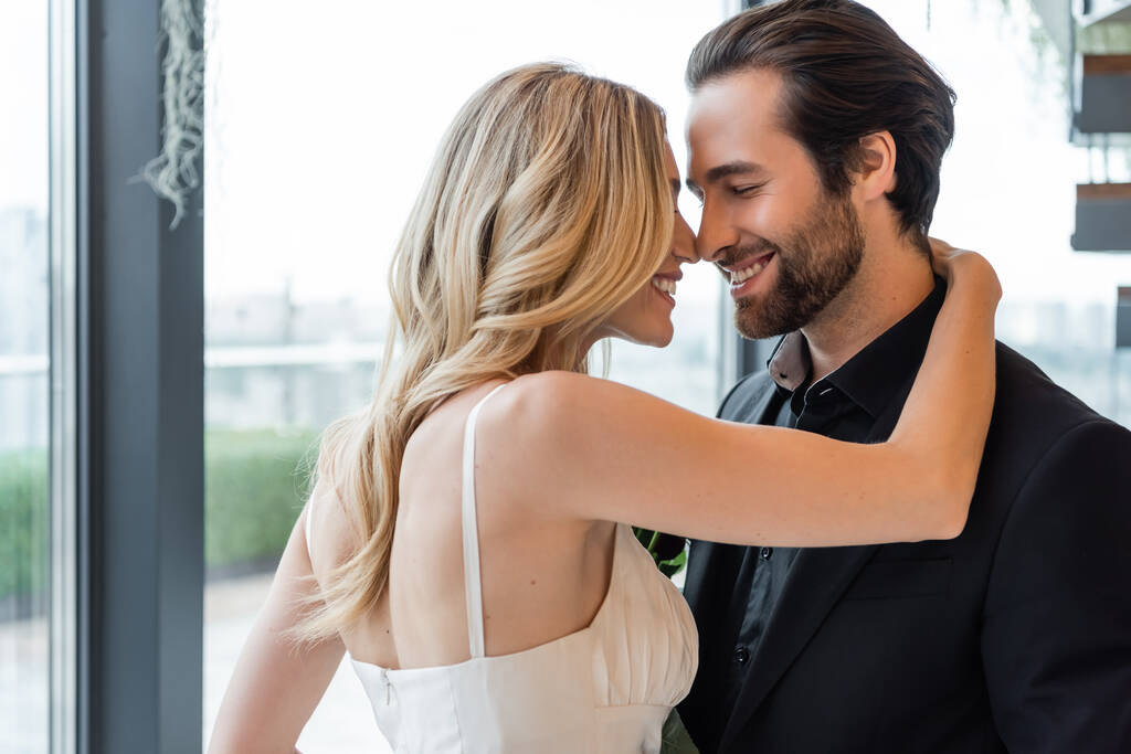 Side view of smiling blonde woman embracing boyfriend in suit in restaurant  - Foto, imagen