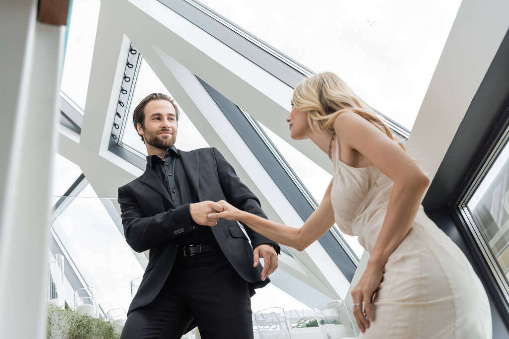 Low angle view of young man in suit holding hand of blonde girlfriend in restaurant  - Foto, afbeelding