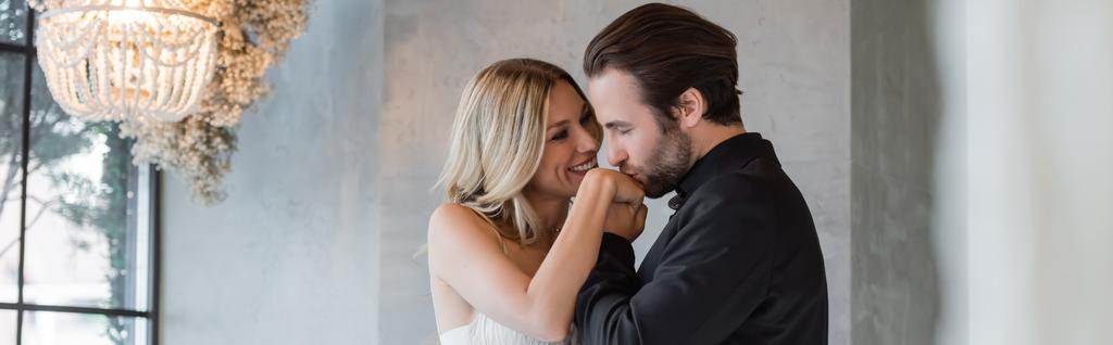Bearded man in suit kissing hand of smiling girlfriend in restaurant, banner  - Photo, Image