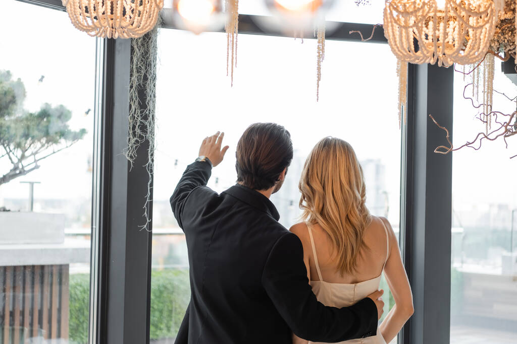 Back view of man in suit hugging girlfriend and pointing with hand in restaurant  - Foto, afbeelding