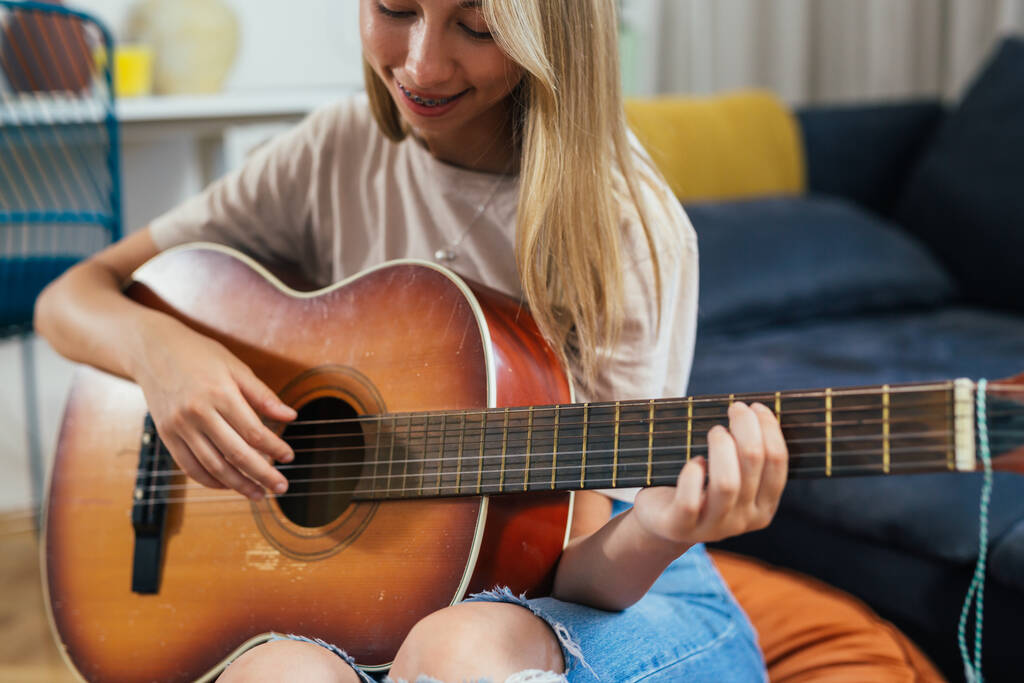 close up of female teenager playing acoustic guitar at home - Foto, afbeelding