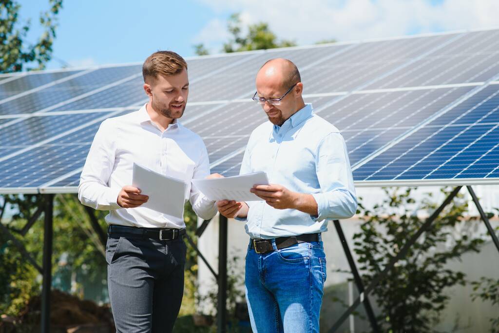 Dwie osoby ściskające dłonie przed panelem słonecznym po zawarciu umowy w sprawie energii odnawialnej. - Zdjęcie, obraz
